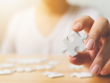 Hand of male trying to connect pieces of white jigsaw puzzle on wooden table. Healthcare for Alzheimer disease, dementia, memory loss, autism awareness and mental health concept