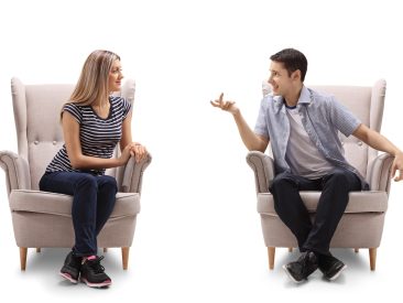 Young woman and a young man sitting in armchairs and talking isolated on white background
